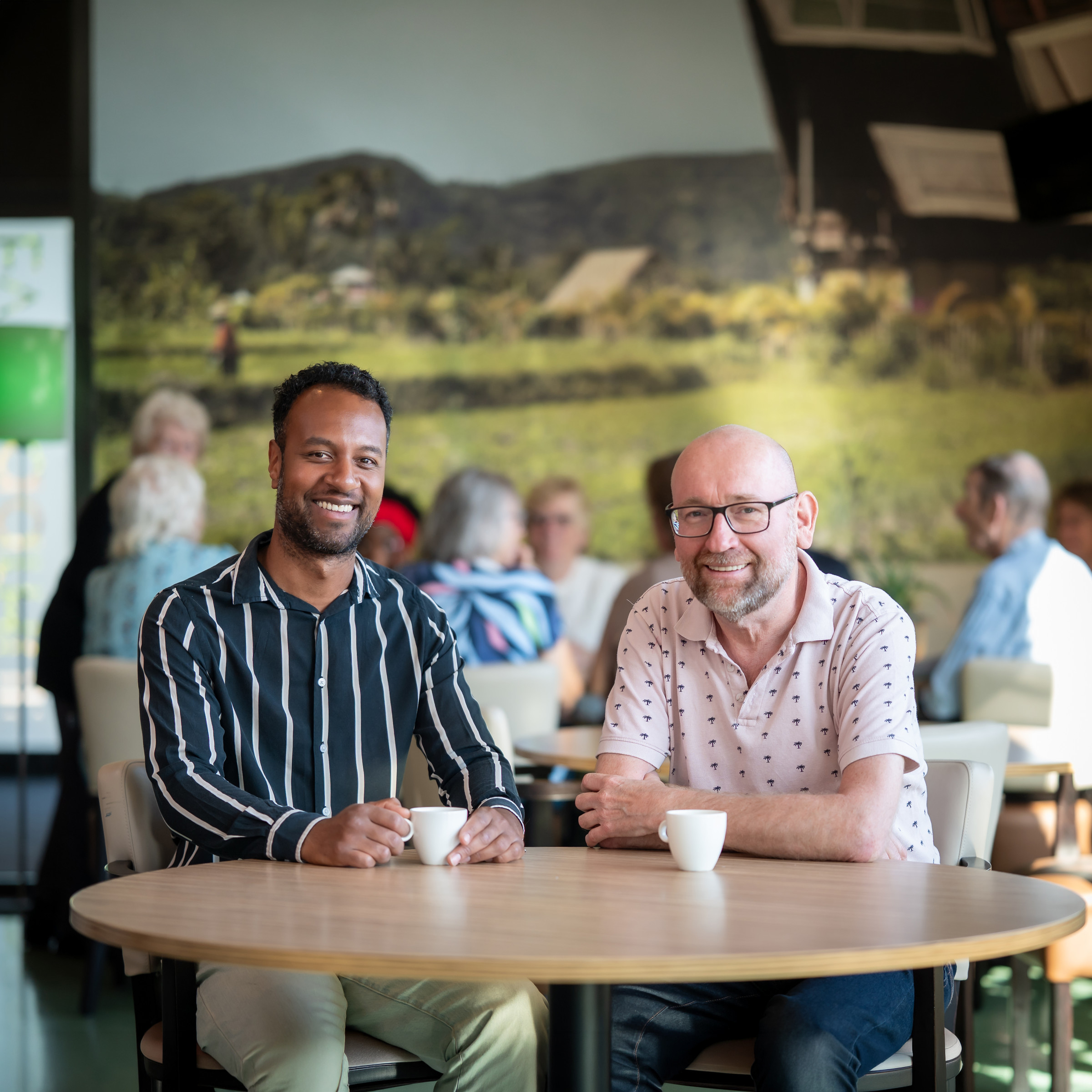 Elimar Evertsz en Henk Westhoff zitten lachend naast elkaar aan een tafel.
