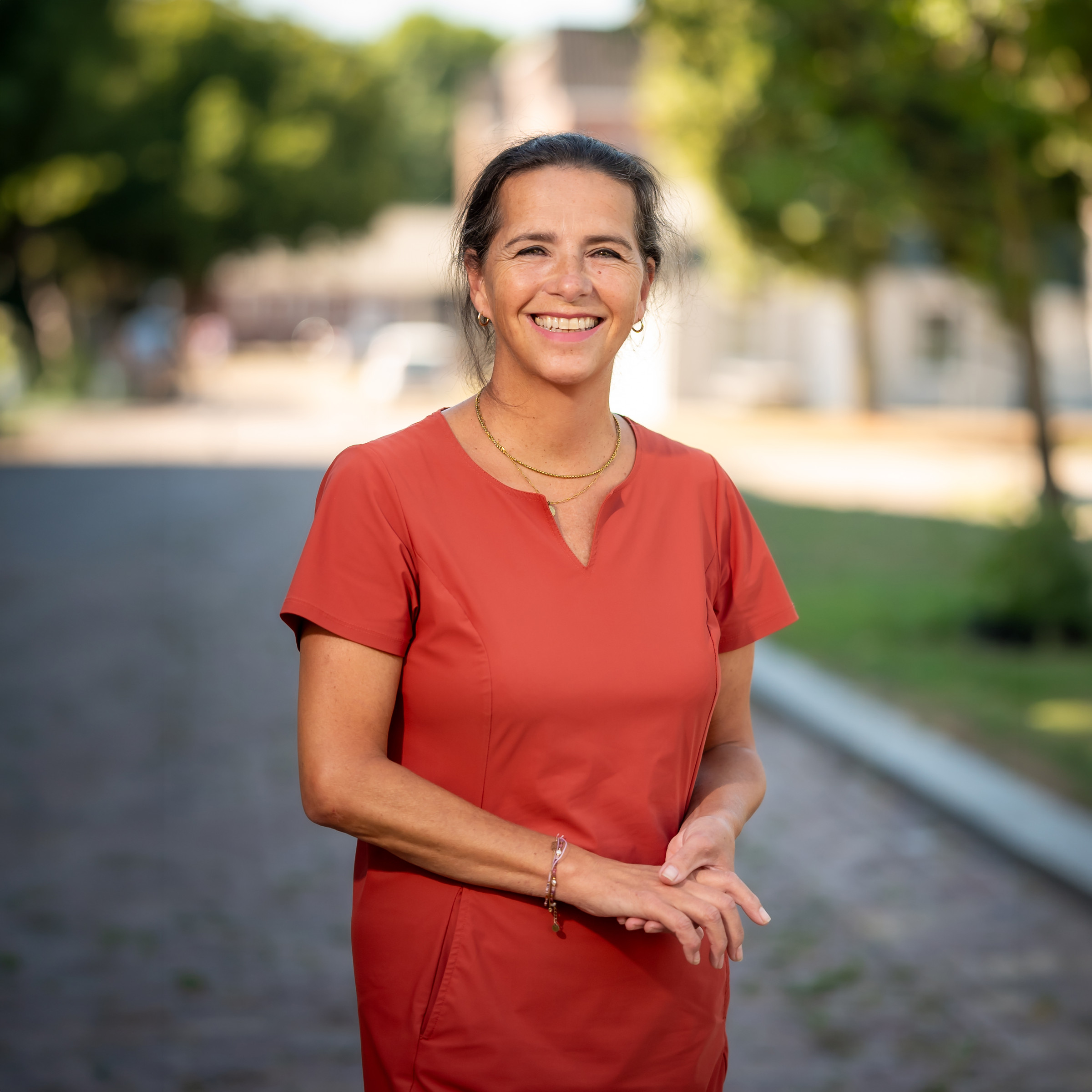 Karin de Bie staat lachend op een pad in een oranje-rode jurk.